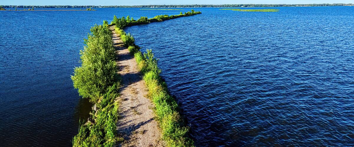 A waterway with a narrow path flanked by greenery, leading to a distant island.