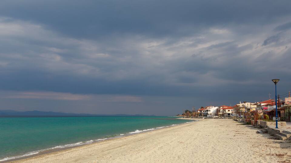 A beach with a row of buildings along the shore and a cloudy sky.