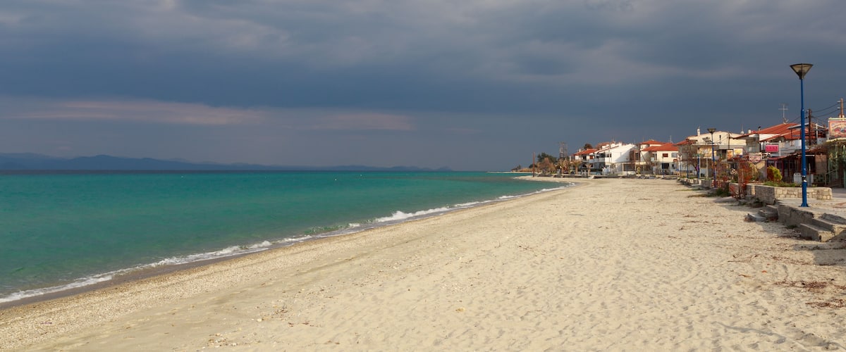 A beach with a row of buildings along the shore and a cloudy sky.