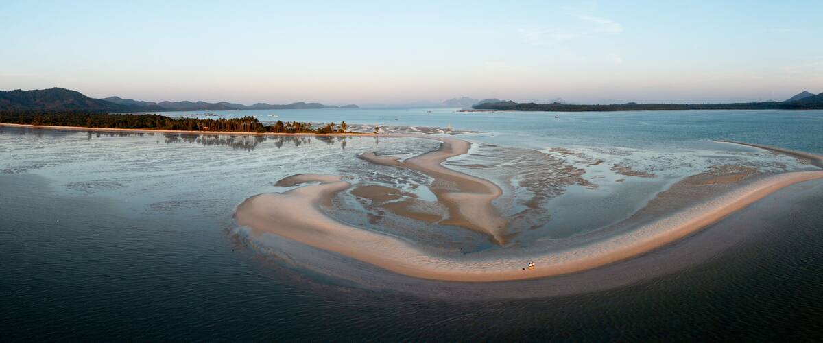 A coastal landscape with a sandy beach, calm waters, and distant mountains.