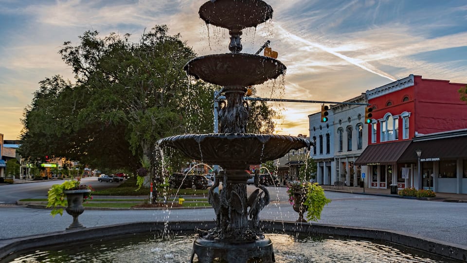 A multi-tiered fountain in a town square with buildings in the background.