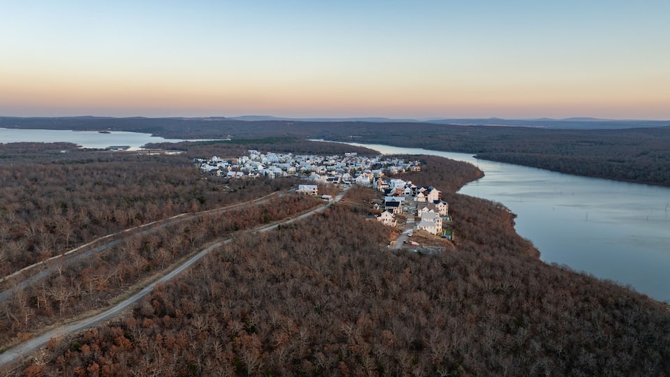 An aerial view of a lakeside town with houses along the shore and a forested area in the foreground.