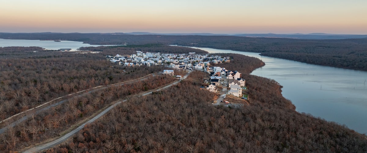 An aerial view of a lakeside town with houses along the shore and a forested area in the foreground.
