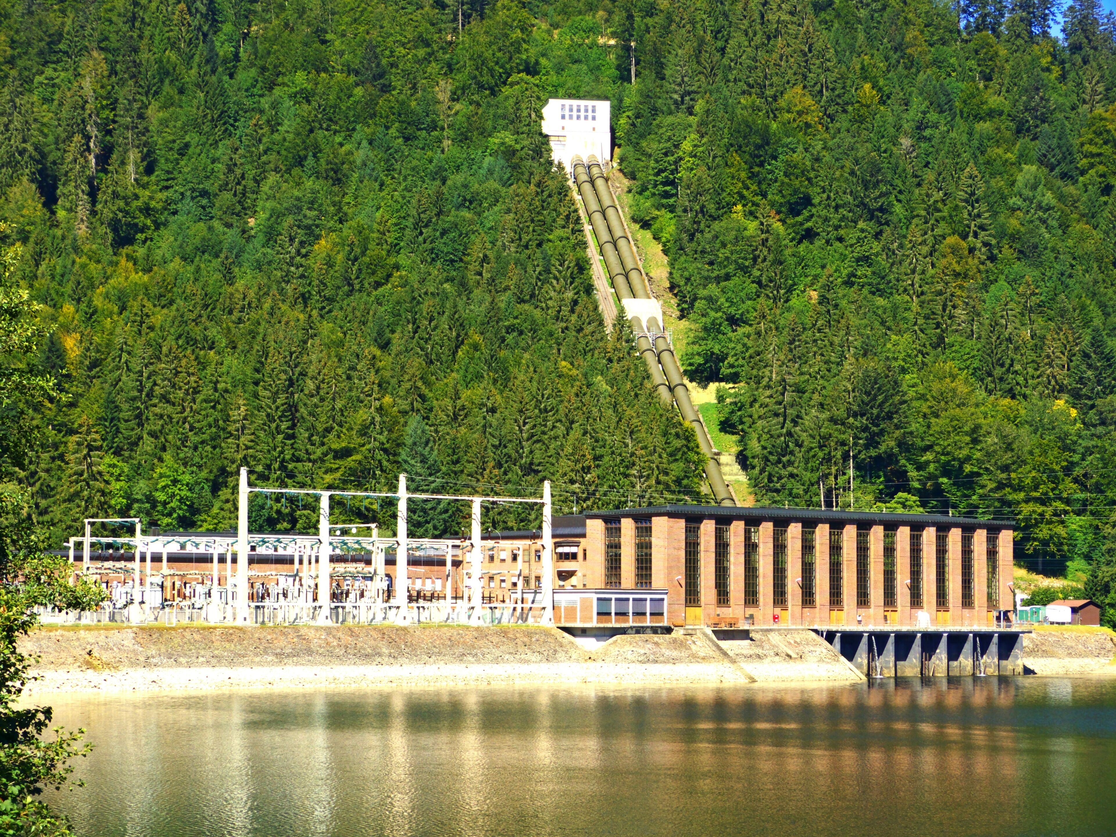 A hydroelectric dam with a large reservoir and a forested hillside in the background.