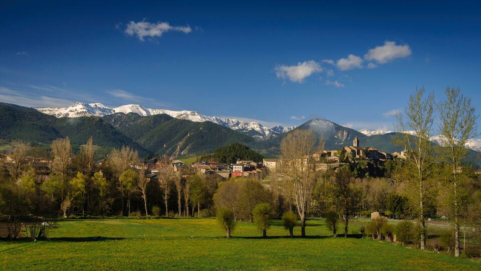 A village nestled in a valley with snow-capped mountains in the background.