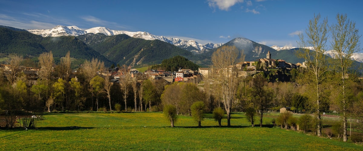 A village nestled in a valley with snow-capped mountains in the background.