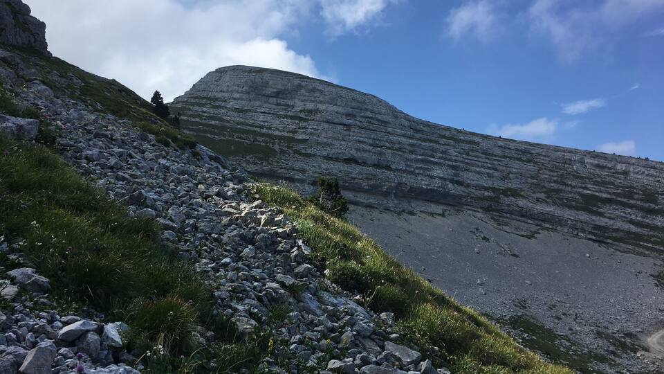 A rocky mountain path with sparse vegetation and a clear sky.