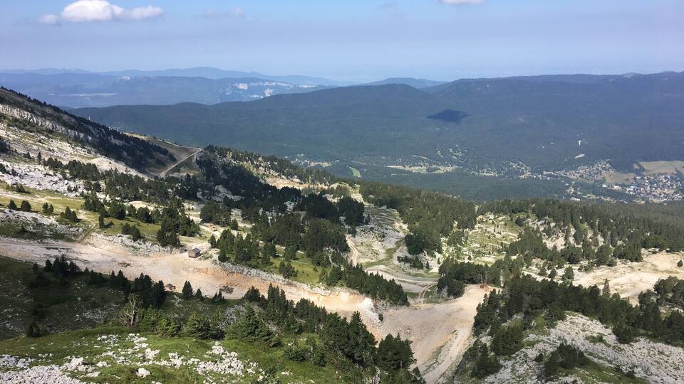 A mountainous landscape with rocky terrain, patches of grass, and scattered trees.