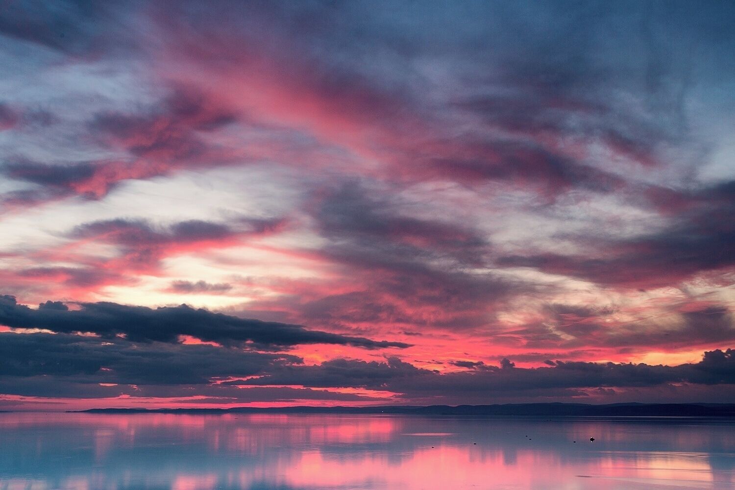 A sunset over a calm body of water with a reflection of the sky.