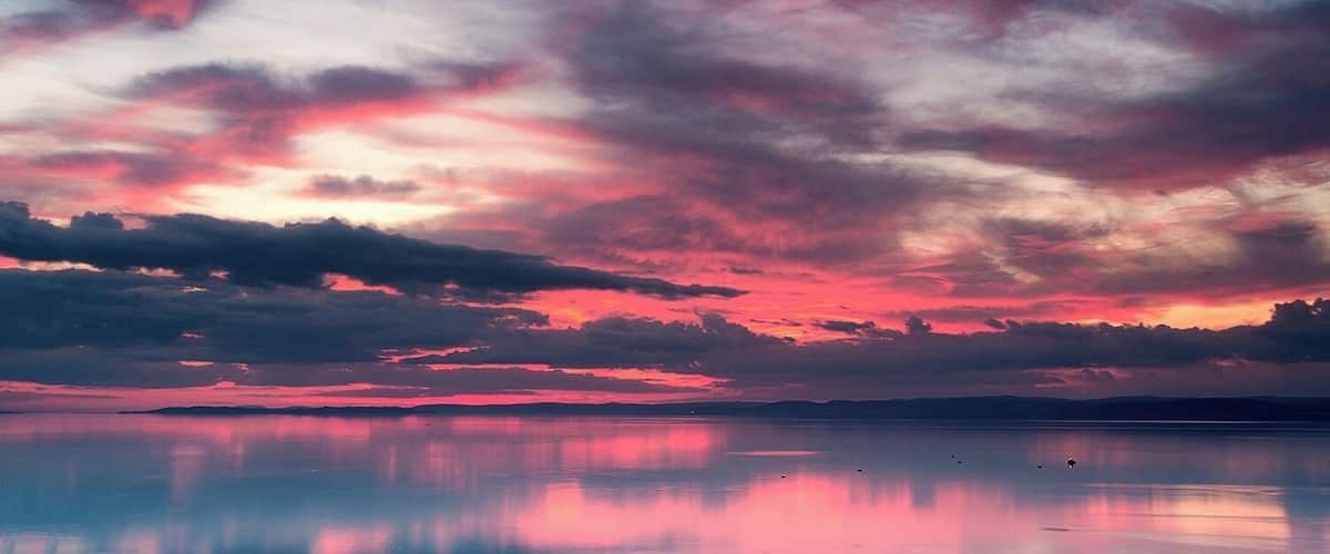 A sunset over a calm body of water with a reflection of the sky.