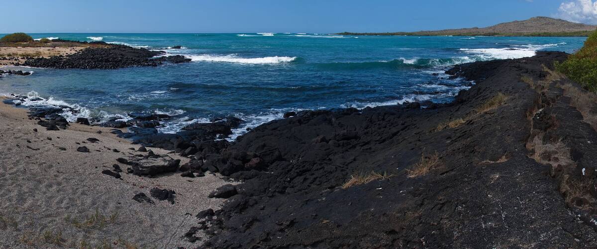 A coastal landscape with a rocky shoreline, waves crashing against the rocks, and a clear blue sky.