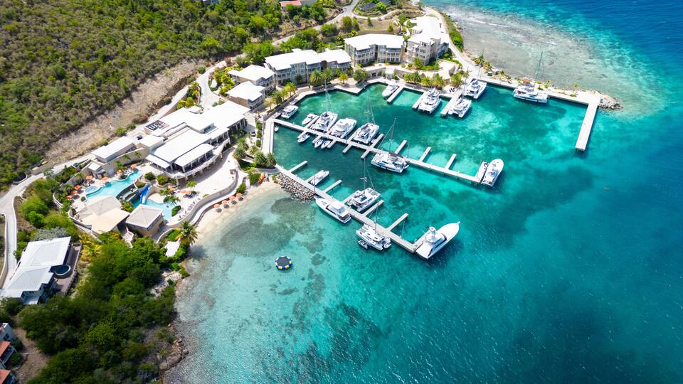 An aerial view of a coastal resort with a marina, swimming pool, and lush greenery.