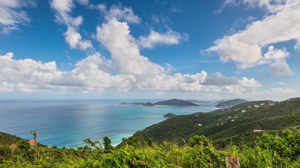 A coastal landscape with a clear sky, lush greenery, and distant islands.