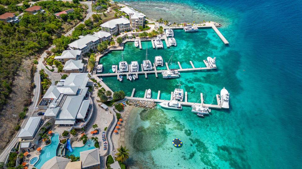 An aerial view of a coastal resort with a marina, swimming pool, and lush greenery.