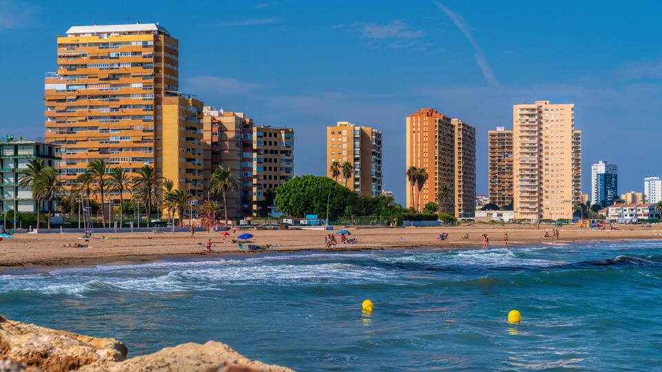 A beach with tall buildings, palm trees, and people enjoying the sand and water.