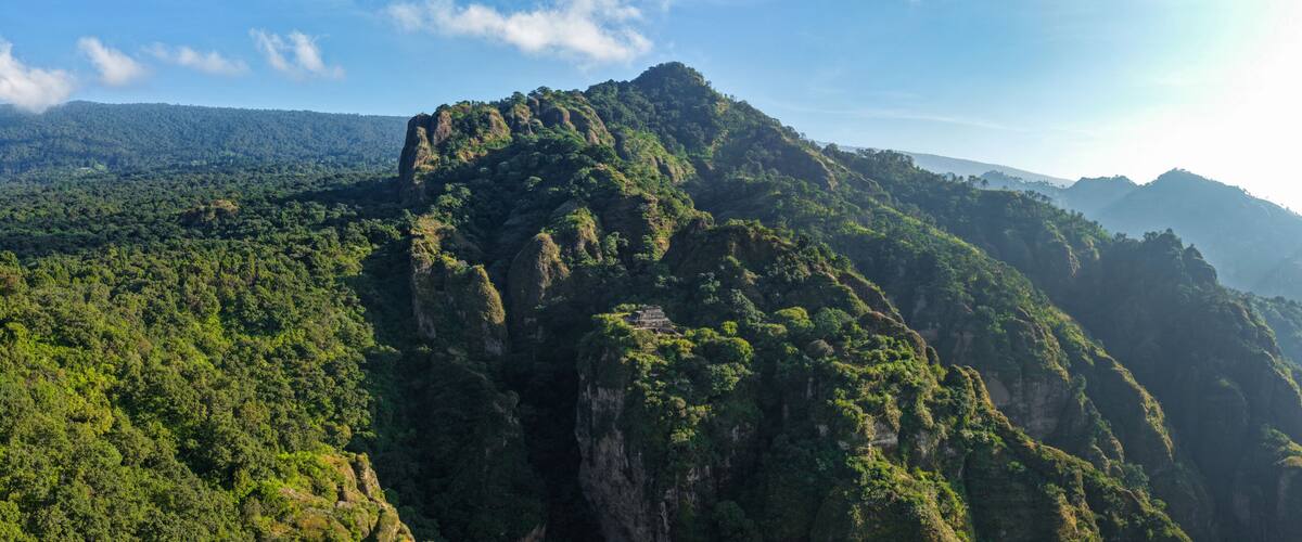 A mountainous landscape with dense green forests and a small ancient structure on a cliff.