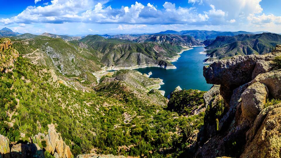 A mountainous landscape with a river, green vegetation, and rocky terrain.