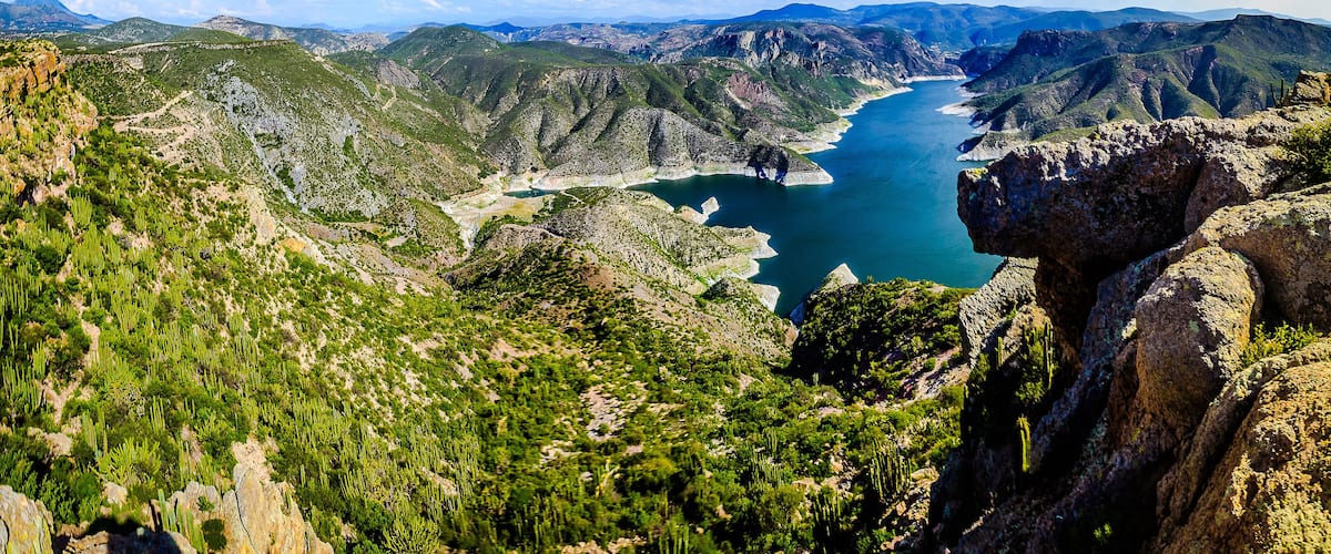 A mountainous landscape with a river, green vegetation, and rocky terrain.
