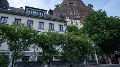 Un bâtiment doté d’une tour horloge, d’une grande formation rocheuse et d’arbres verdoyants.