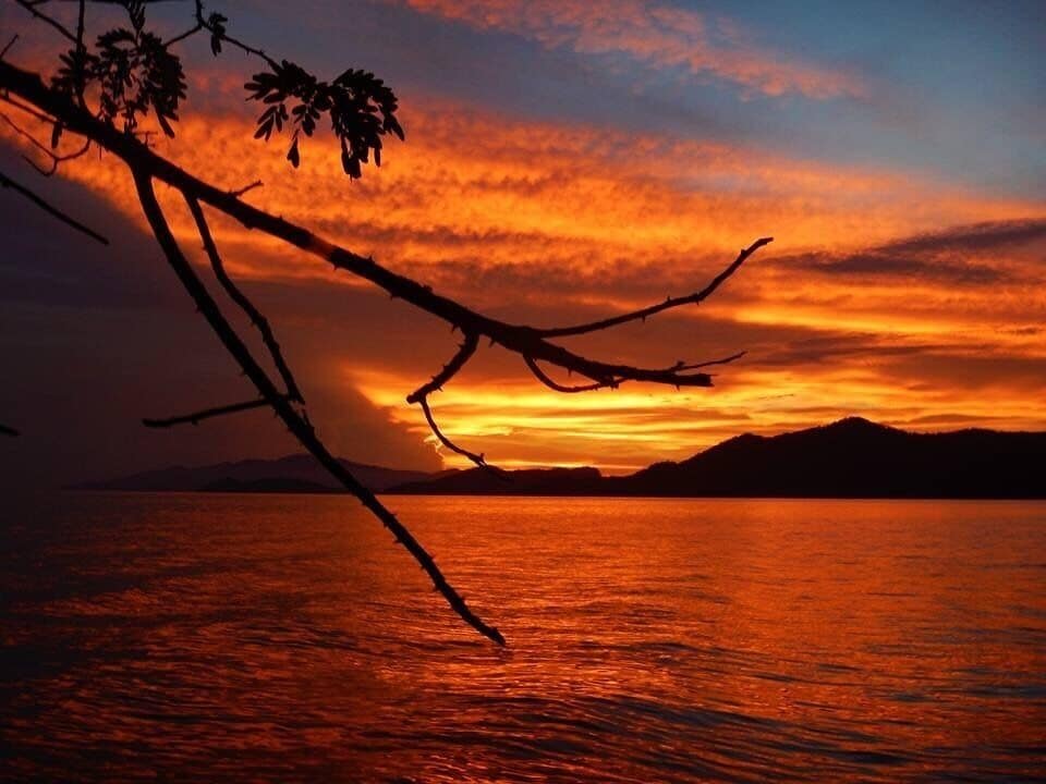 A sunset over a body of water with silhouetted mountains in the background.