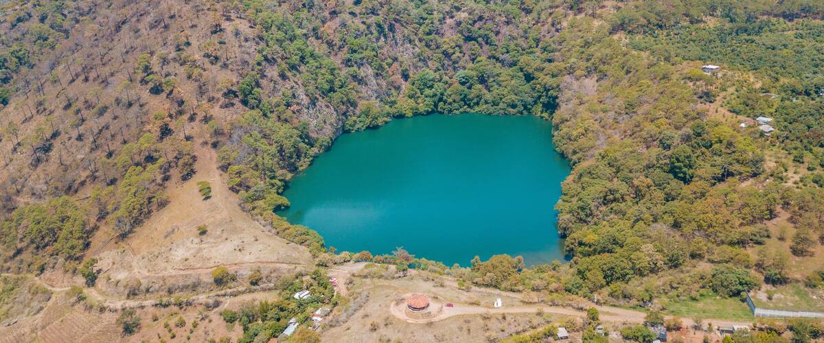 A lake surrounded by forested hills with a small building near the water's edge.