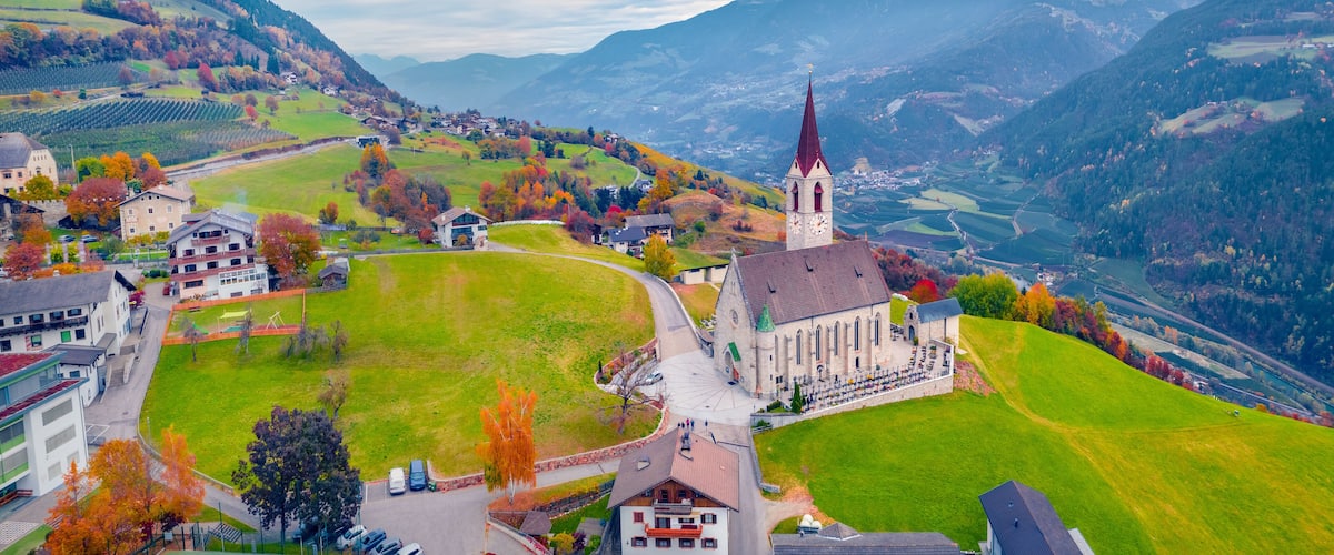 A town with a church, surrounded by mountains and autumn-colored trees.