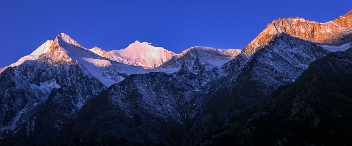 A mountain range with snow-capped peaks under a clear blue sky.