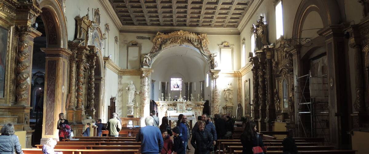 An ornate church interior with wooden pews, a high ceiling with intricate designs, and statues.