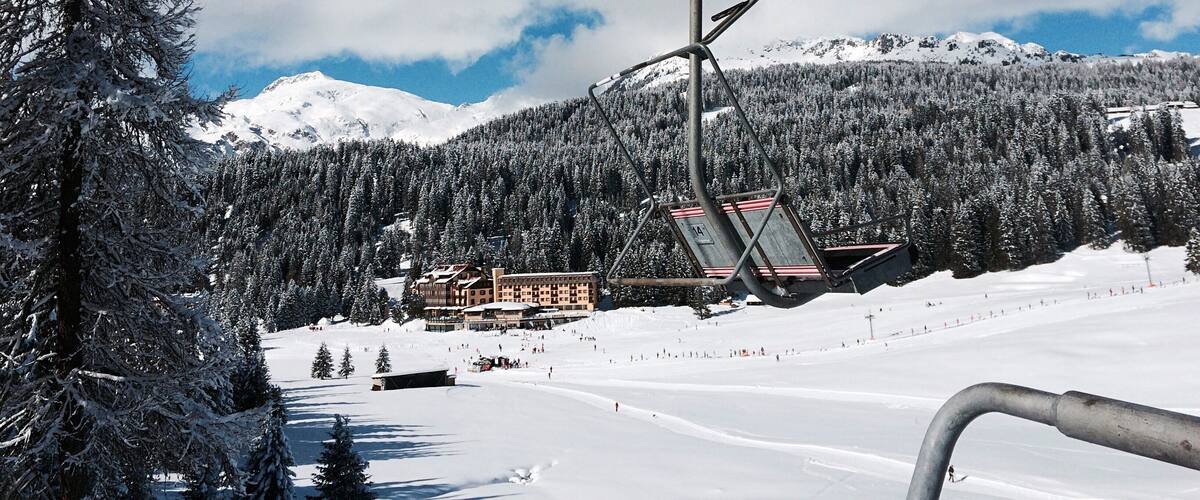 A ski lift in a snowy mountainous area with a lodge and snow-covered trees.