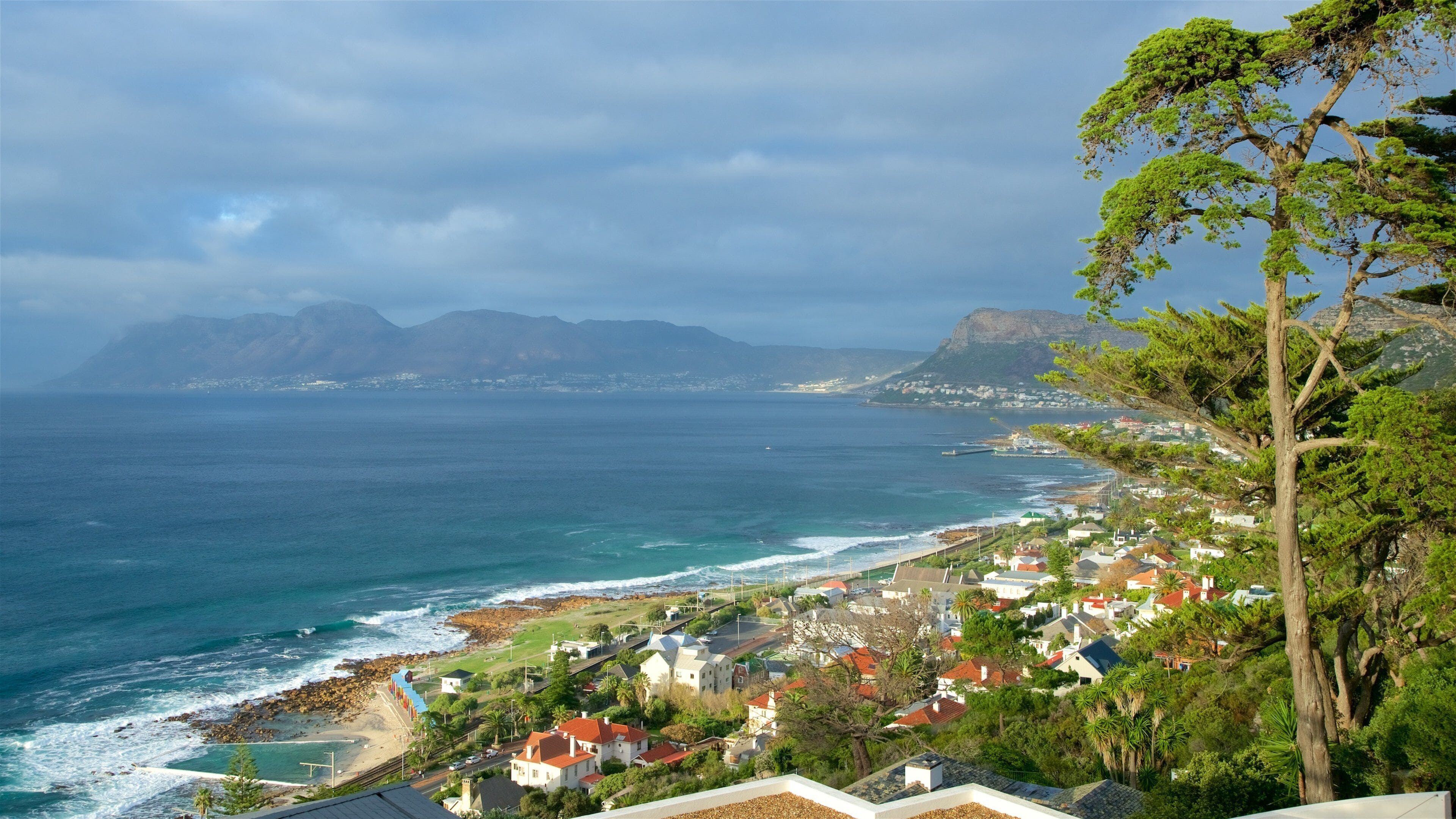 Uma vila costeira com casas, uma praia e montanhas ao fundo.