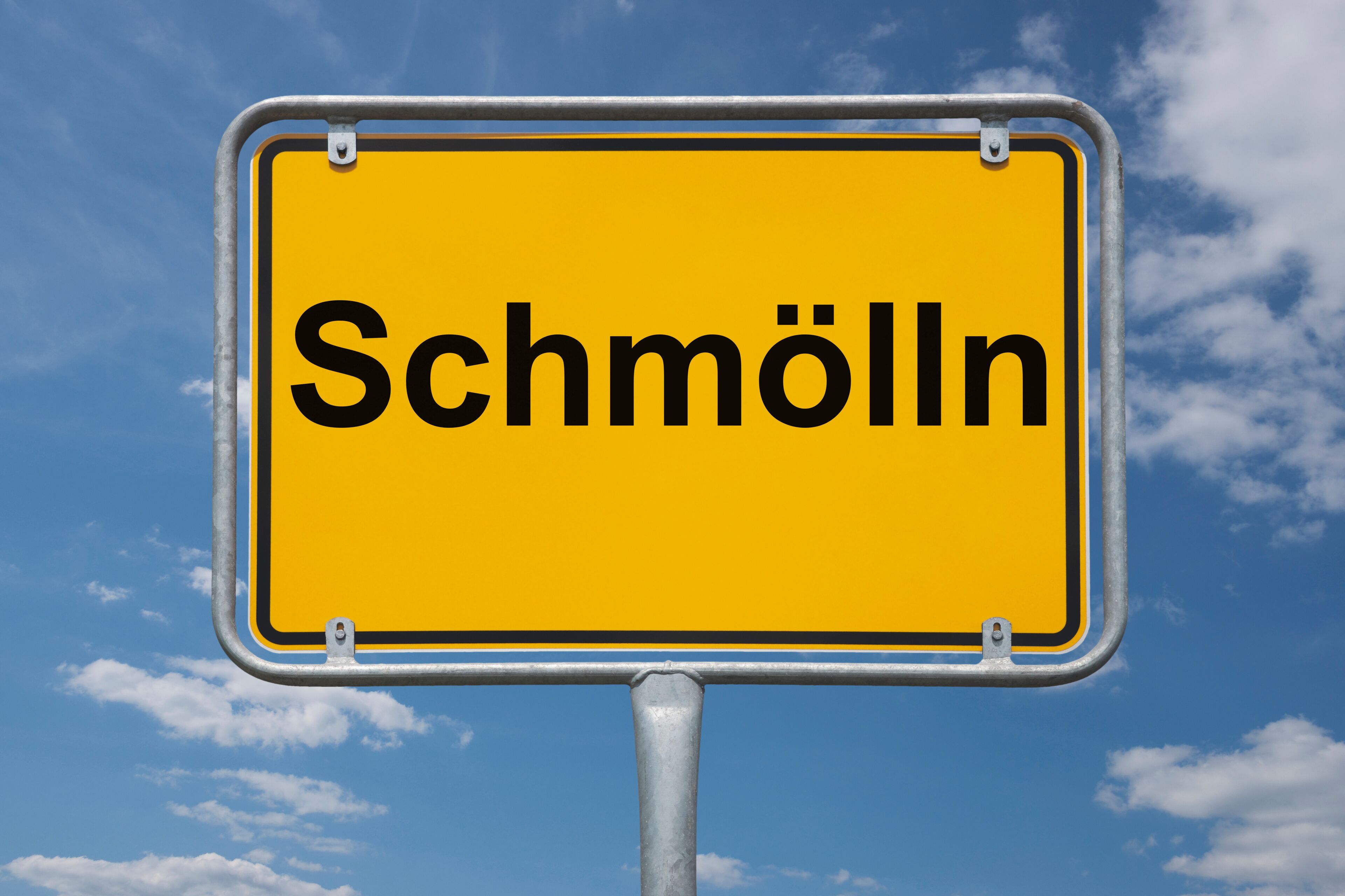 A yellow sign with the word "Schmölln" against a blue sky with clouds.