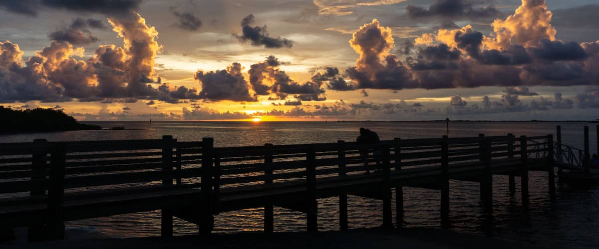 A sunset over a body of water with a wooden pier and a distant shoreline.