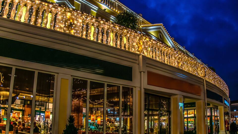 A brightly lit building with a balcony adorned with string lights and a Christmas tree.