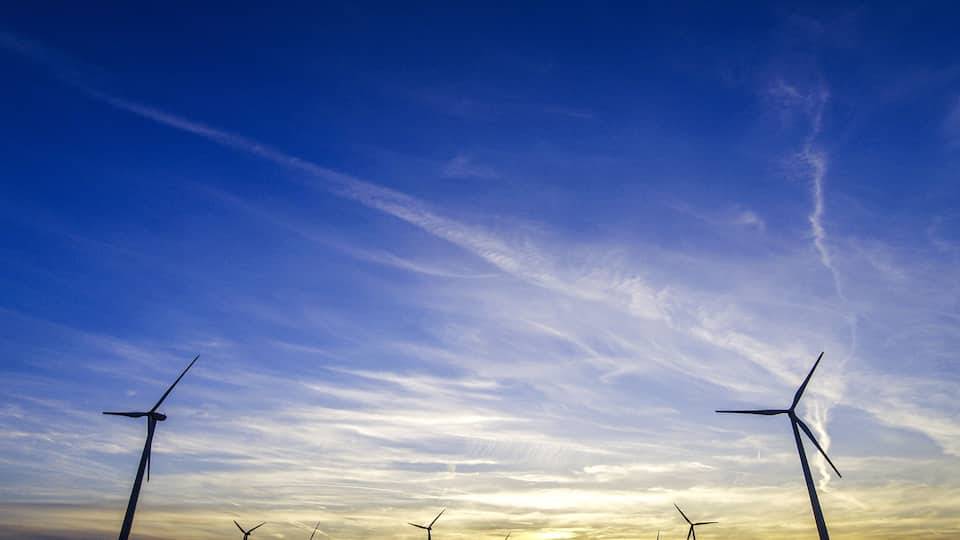 A sunset over a wind farm with multiple wind turbines.
