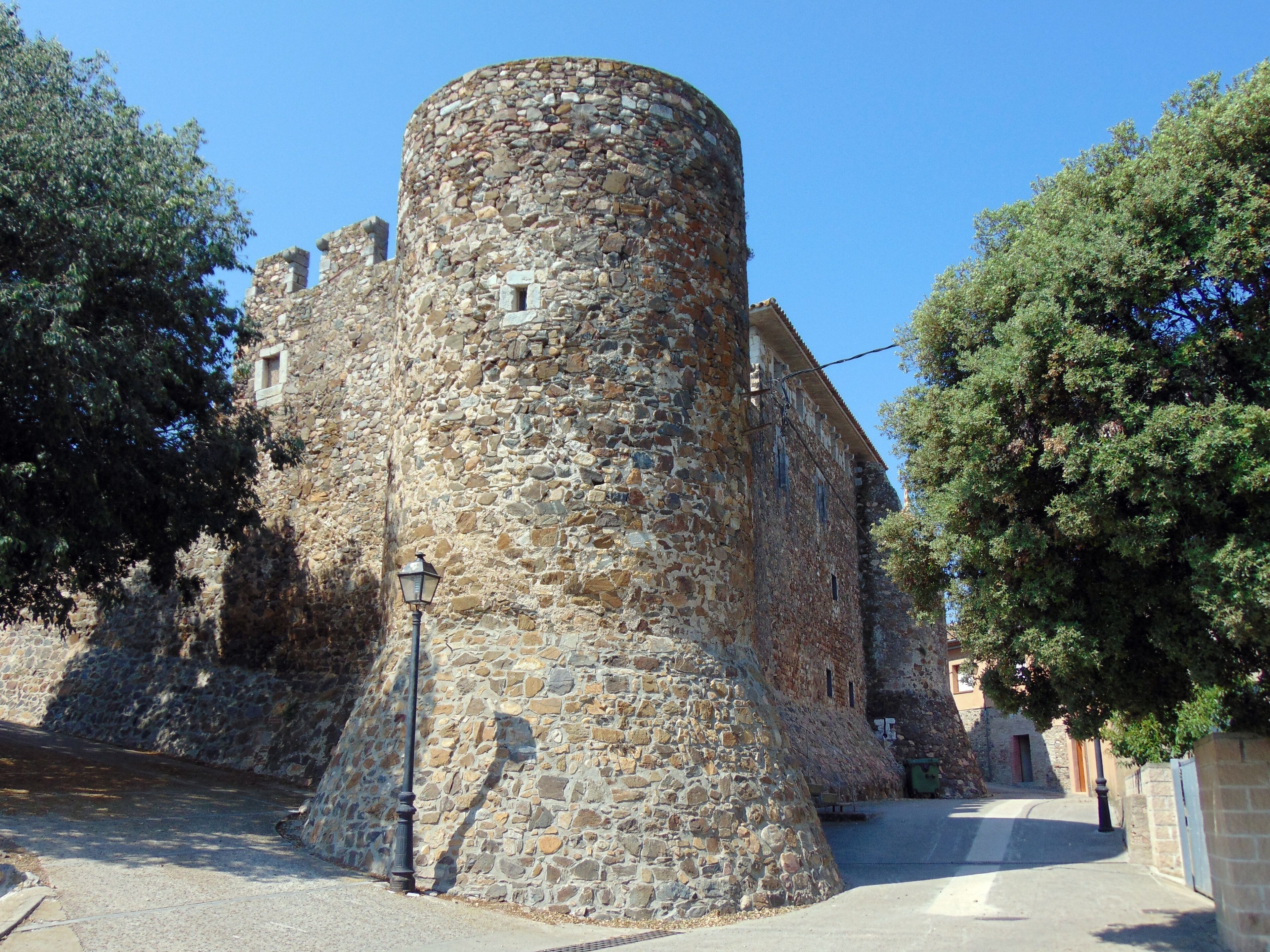 A stone tower with a rounded top, surrounded by trees and a street.