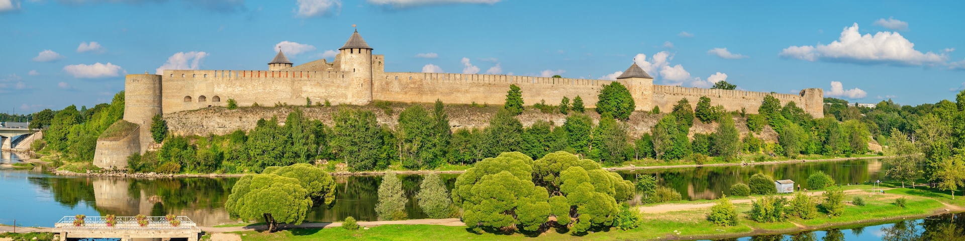A historic castle by a calm river with lush greenery and a clear sky.