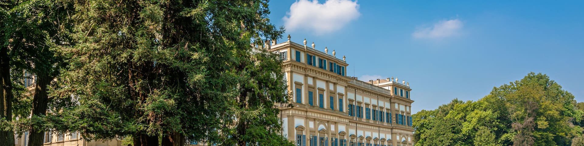 A large, classical building with a grand staircase and lush green lawns.