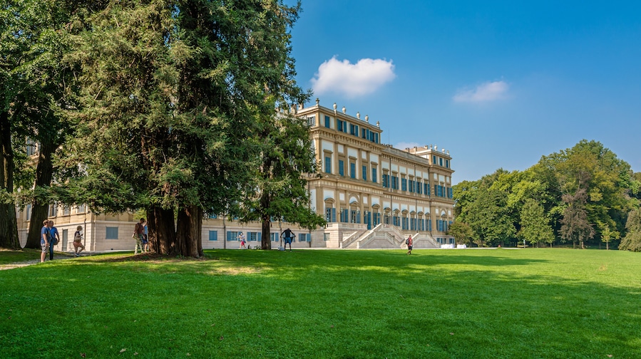 A large, classical building with a grand staircase and lush green lawns.