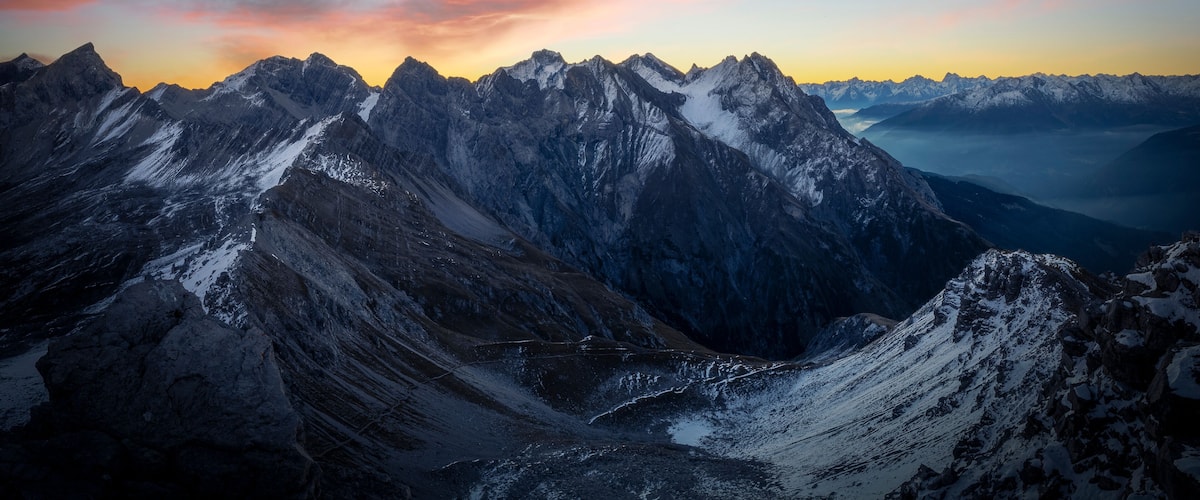 A mountain range with snow-capped peaks and a sunset sky.