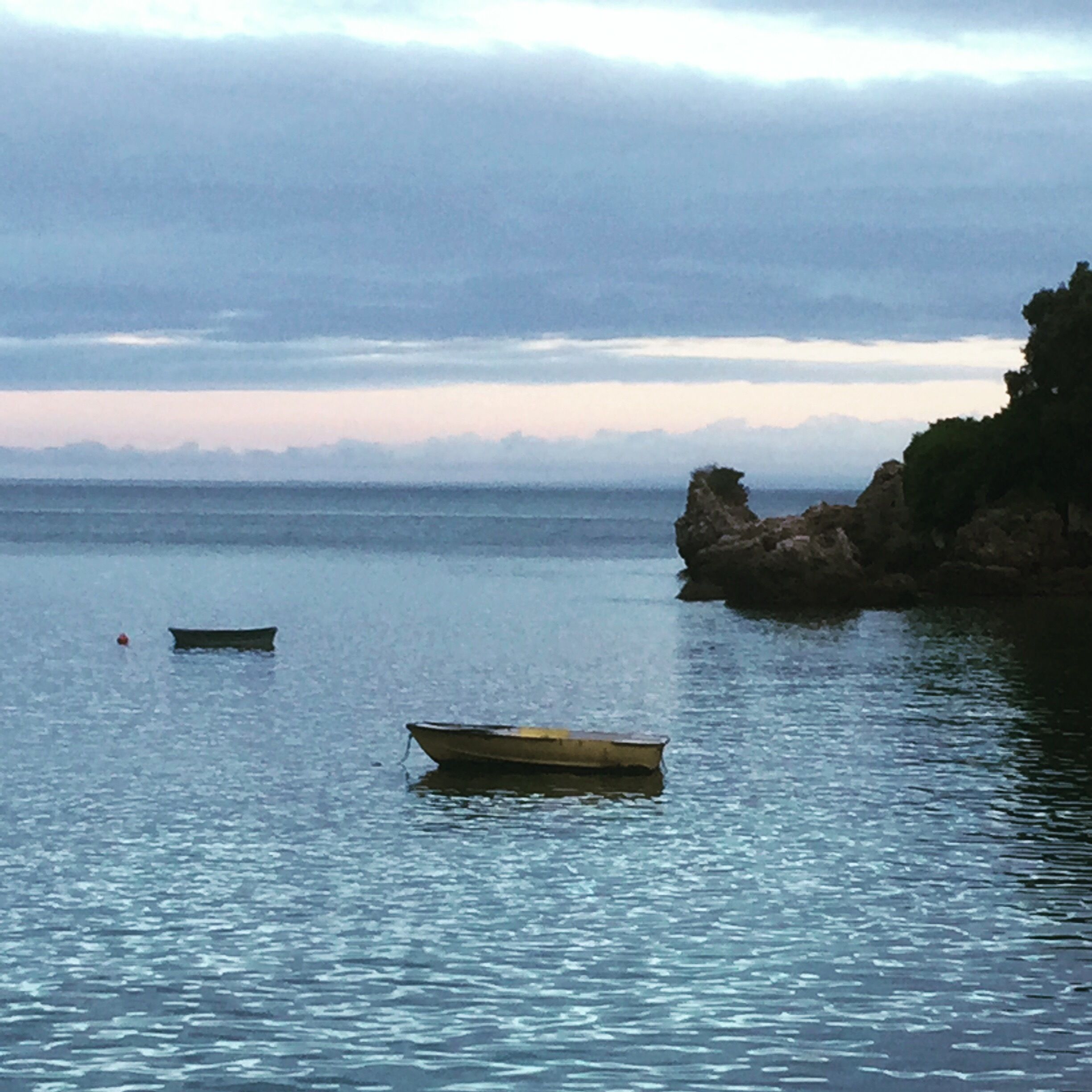 Calm water with two small boats and a rocky outcrop in the distance.