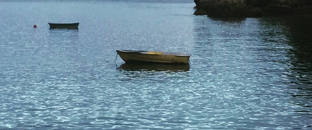 Calm water with two small boats and a rocky outcrop in the distance.