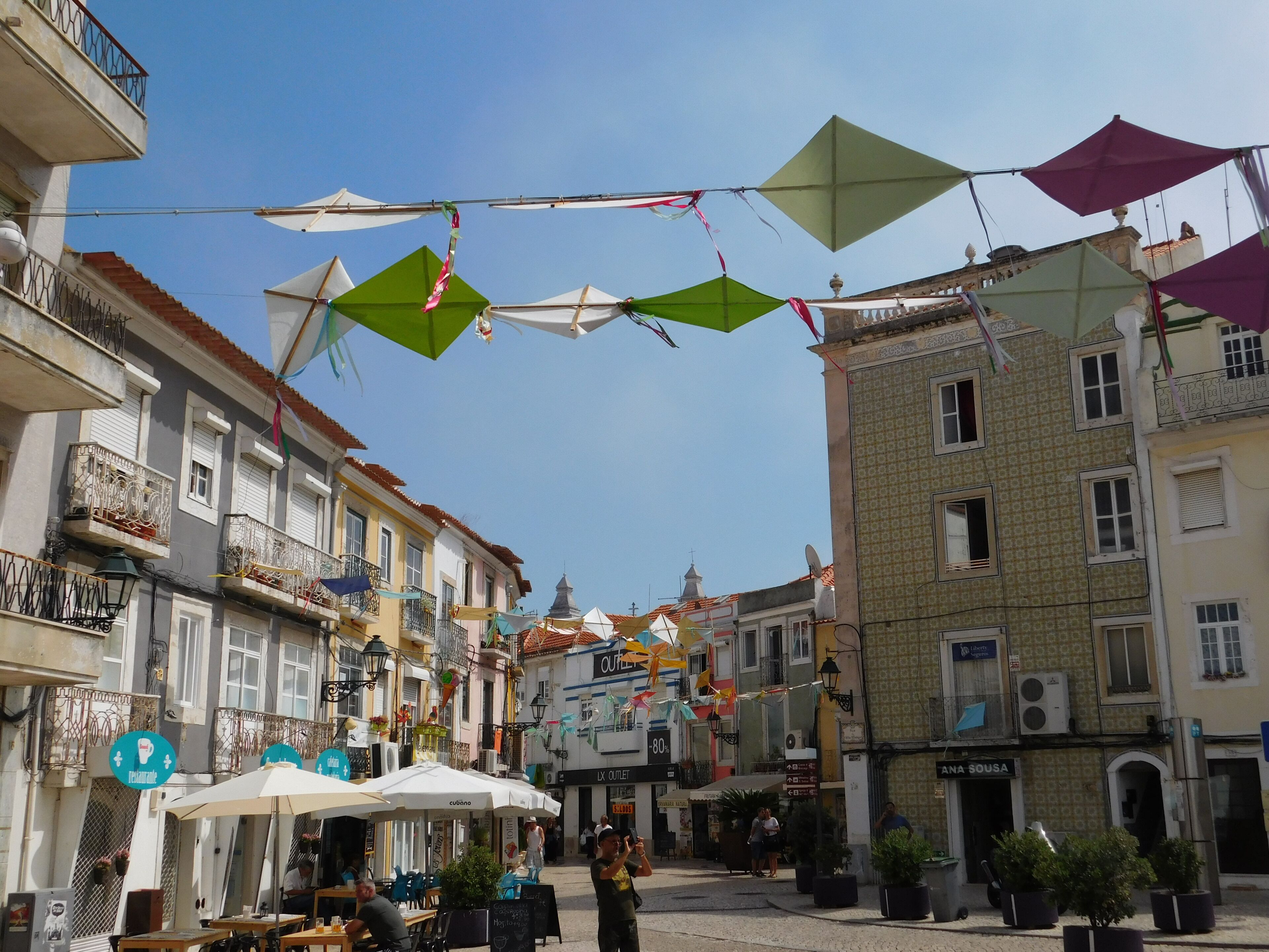 A street with buildings, outdoor seating, and hanging decorations.