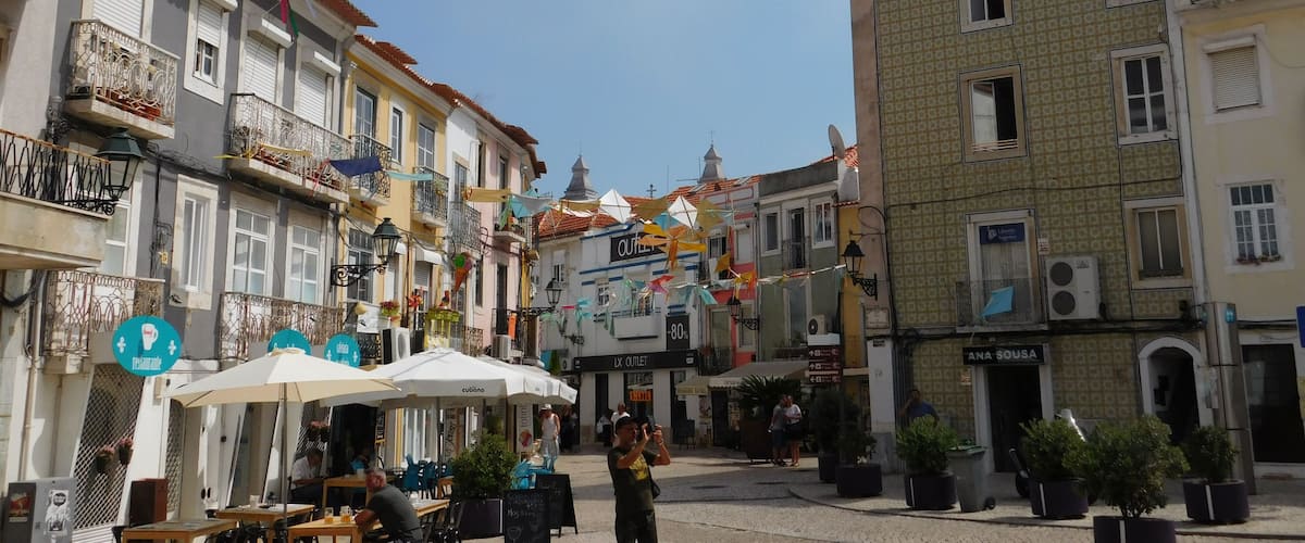 A street with buildings, outdoor seating, and hanging decorations.