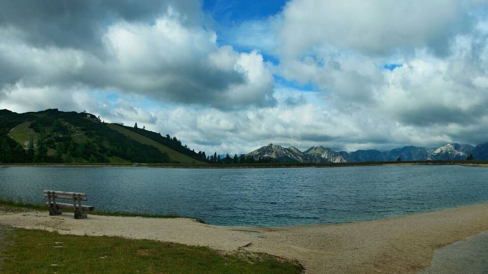 A lake with mountains in the background and a bench on the shore.