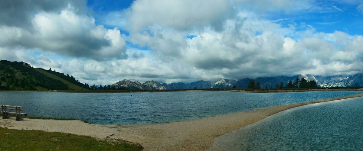 A lake with mountains in the background and a bench on the shore.