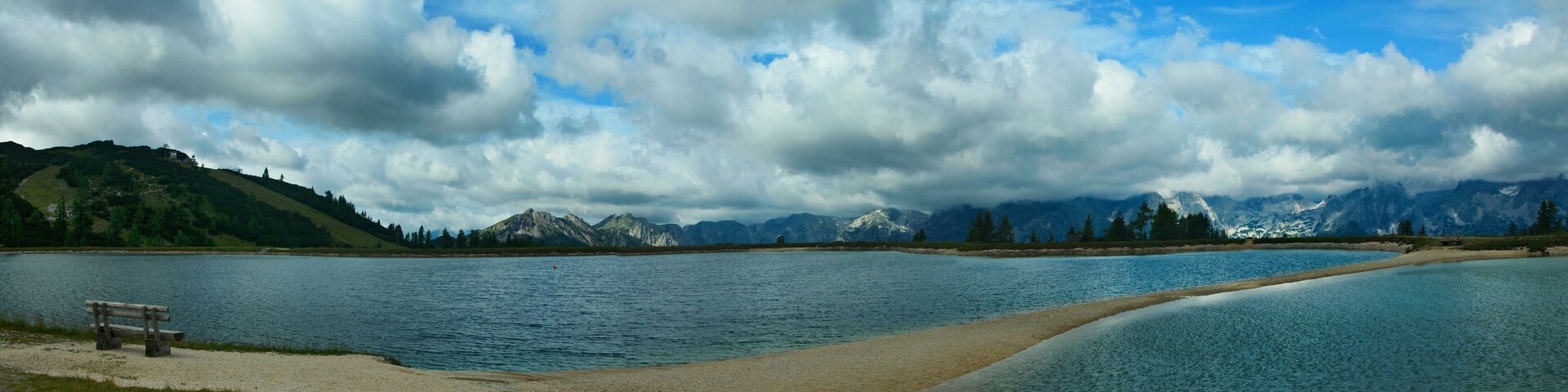 A lake with mountains in the background and a bench on the shore.