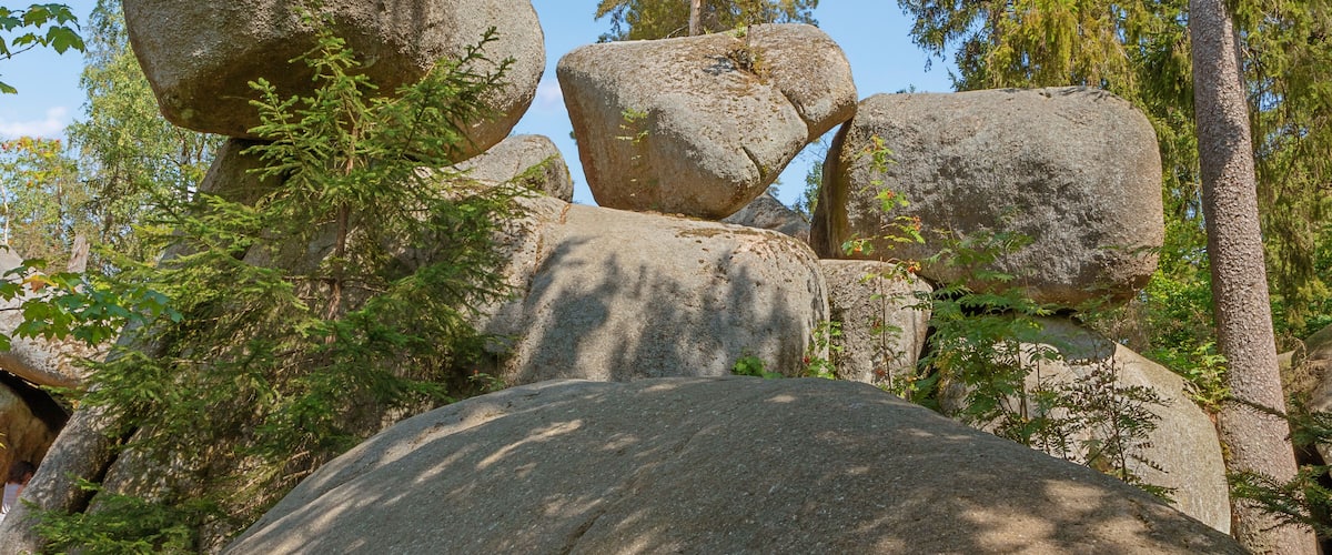 Large boulders balanced on smaller rocks, surrounded by trees and greenery.