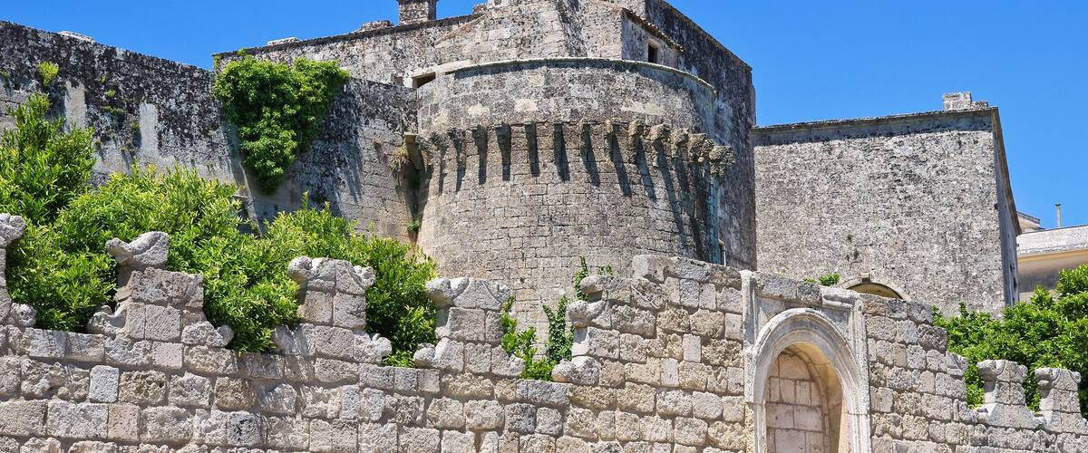 A historic stone wall with a round tower and an arched entrance.