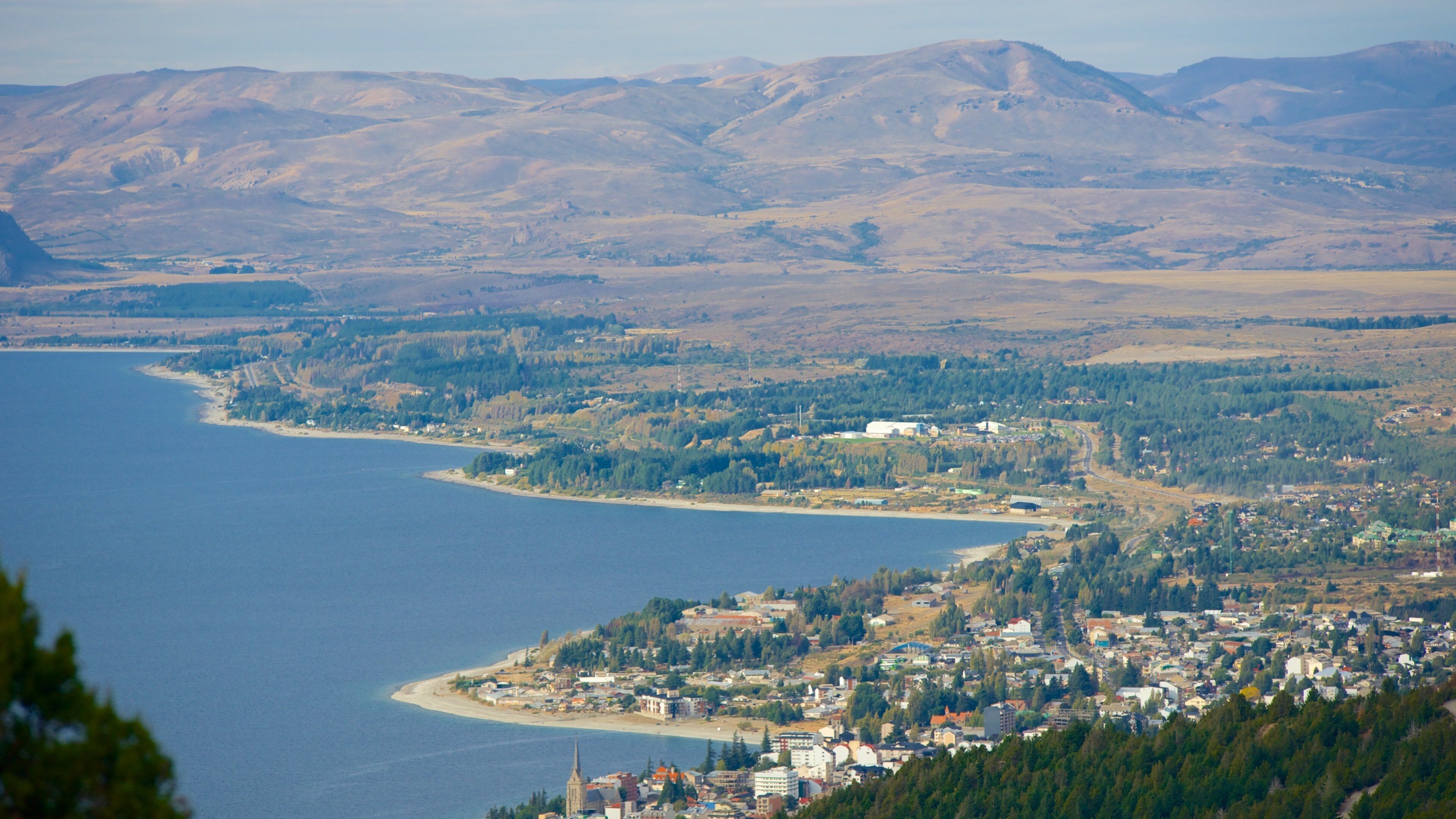 A coastal town with a beach, surrounded by mountains and dense forests.