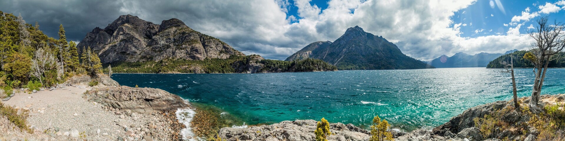 Paisagem montanhosa com um lago límpido, rodeada por terreno rochoso e vegetação escassa.